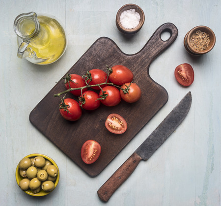 Preparation of salad with tomatoes, olives, butter and various seasonings, ingredients are lined around the cutting board on a blue wooden backgroundの写真素材