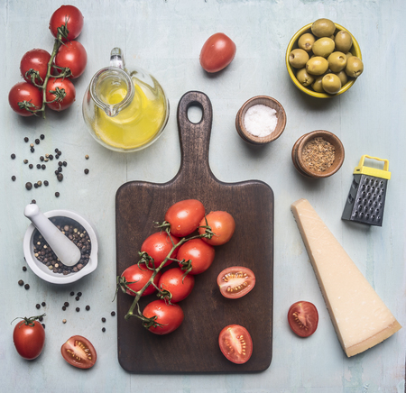 Preparation of salad with tomatoes, olives, butter and various seasonings, ingredients are lined around the cutting board on a blue wooden backgroundの写真素材