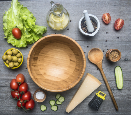 Ingredients  preparation healthy food, lettuce, olives, cherry tomatoes, cucumbers, parmesan cheese, grater, condiments and olive oil in a decanter, lined around a wooden salad bowl, frame, space textの写真素材