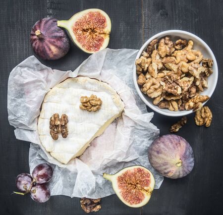 appetizing camembert cheese, with walnuts, figs and a branch of ripe dark grapes, on a rustic wooden dark wooden background, top viewの写真素材
