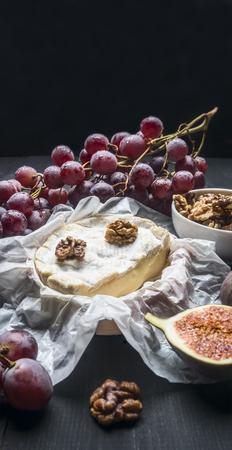 appetizing camembert cheese, with walnuts, figs and a branch of ripe dark grapes, on a rustic wooden dark wooden background, top view place for textの写真素材