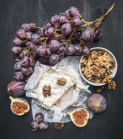 appetizing camembert cheese, with walnuts, figs and a branch of ripe dark grapes, on a rustic wooden dark wooden background, top viewの写真素材