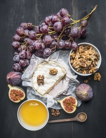 appetizing camembert cheese, with walnuts, figs and a branch of ripe dark grapes, on a rustic wooden dark wooden background, top viewの写真素材