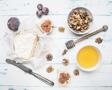 Camembert cheese on old wooden table with a bowl of walnuts, honey, a vintage table knife, cut figs and grapes, top viewの写真素材