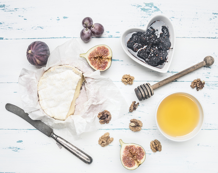 Camembert cheese on old wooden table with a bowl of walnuts, honey, a vintage table knife, cut figs and grapes, top viewの写真素材