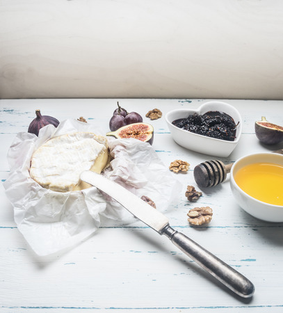 Camembert cheese on white wrapping paper, with jam, walnuts and honey, fresh figs, on a rustic wooden background place for textの写真素材