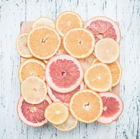 sliced oranges, lemons and grapefruits, on a wooden tray, against the background of a wooden table, the concept of useful citrus fruitsの写真素材