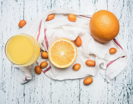Healthy foods morning juice from oranges and kumquat, fruits are laid out on a white napkin, a glass filled with juice, on a wooden rustic backgroundの写真素材