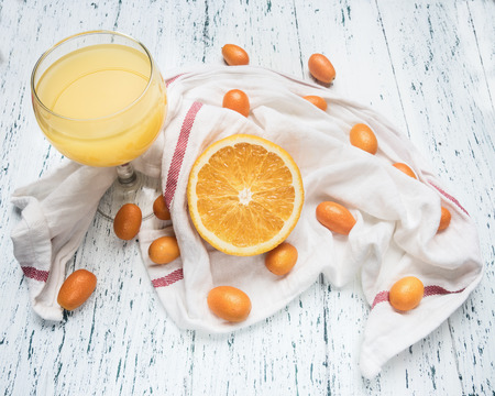 Healthy foods morning juice from oranges and kumquat, fruits are laid out on a white napkin, a glass filled with juice, on a wooden rustic backgroundの写真素材