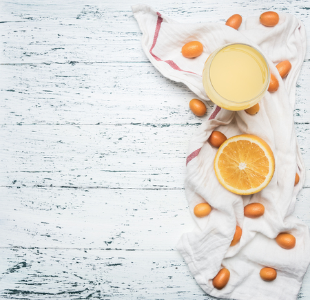 Healthy foods morning juice from oranges and kumquat, fruits are laid out on a white napkin, a glass filled with juice, on a wooden rustic background, space for text, a borderの写真素材