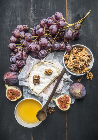 concept of appetizers for wine, camembert cheese, dark grapes, walnuts and figs with honey, on a wooden rustic backgroundの写真素材