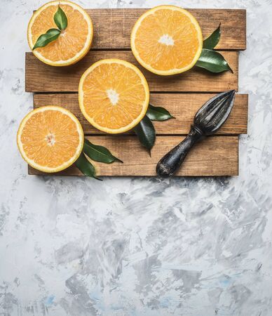 fresh cut oranges with leaves and a wooden crush for fruit, on a rustic wooden tray, top view, space for textの写真素材
