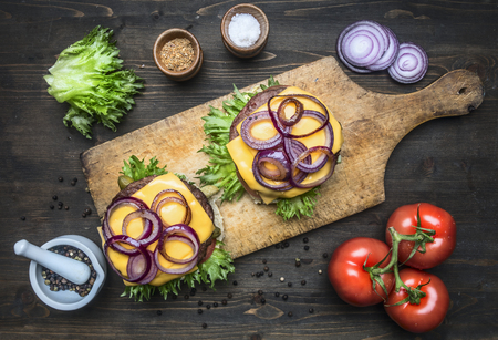 two appetizing juicy home burger with beef, salad, pickled cucumbers, cheese and onions, tomatoes, bun with sesame, on a vintage cutting board, top viewの写真素材