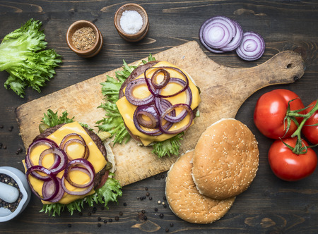 two appetizing juicy home burger with beef, salad, pickled cucumbers, cheese and onions, tomatoes, bun with sesame, on a vintage cutting board, top viewの写真素材