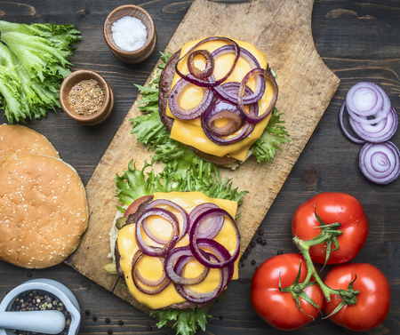 appetizing homemade burgers with a juicy beef chop, red onion, cheese, salad and tomatoes, on a vintage cutting board, top view, close upの写真素材
