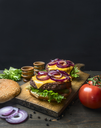 Appetizing homemade burgers with a juicy beef chop, red onion, cheese, salad and tomatoes, on a vintage cutting board, close up, space for textの写真素材