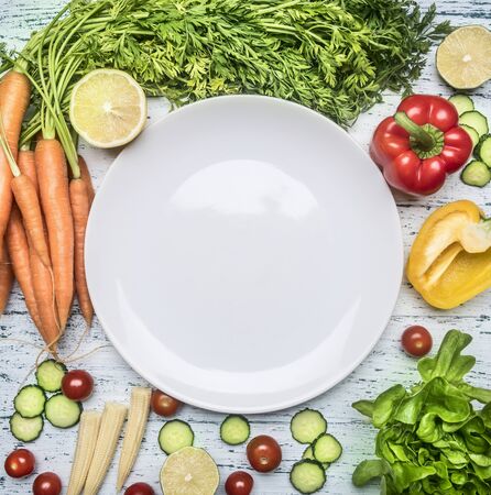 Ingredients for cooking salad cherry tomatoes, lettuce, peppers, spices and oil laid out around a white plate on wooden rustic background top view close up, space for textの写真素材