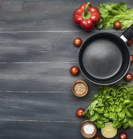 Cooking a vegetarian dinner, red and yellow bell peppers, salad, wooden spoon, cherry tomatoes, condiments,lime, black cooking pot, lined on a wooden rustic background space for textの写真素材