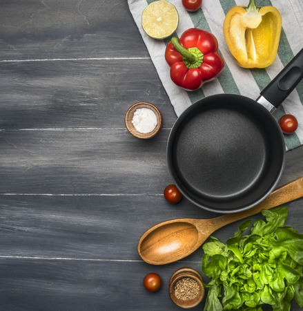 cooking a vegetarian dinner, red and yellow bell peppers, salad, wooden spoon, cherry tomatoes, condiments, lime, black cooking pot, lined on a wooden rustic background space for textの写真素材