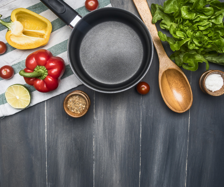 concept cooking veggie food, lettuce cookie, cherry tomatoes, bell peppers, lime, seasonings, wooden spoon, lined around a black pan, on a wooden rustic background, space for textの写真素材