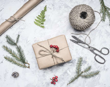 gift for a new year or Christmas, next to it is a roll of paper, vintage scissors, twigs of a christmas trees and berries of a mountain ash, on rustic background, top viewの写真素材