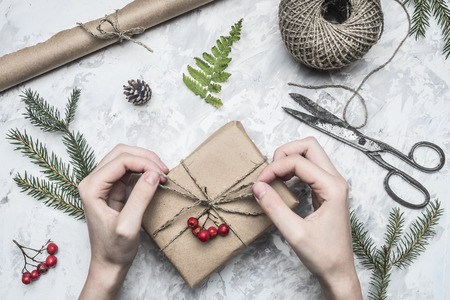 girl wraps a gift for a new year or Christmas, next to it is a roll of paper, vintage scissors, twigs of a christmas trees and berries of a mountain ash, on a rustic background, top viewの写真素材