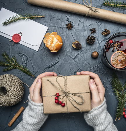 girl in a warm winter sweater holds a gift for a new year or Christmas, there is a mug of mulled wine, an envelope with congratulations with a seal, mandarins and fir branches on a rustic backgroundの写真素材