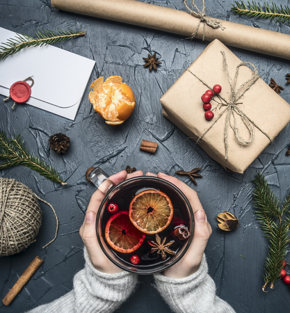 girl holding a mulled wine cup, an envelope lie next to her, a gift for a new year or Christmas, a wrapping paper, fir branches, mandarins and cinnamon sticks, on a rustic background, top viewの写真素材