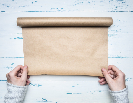 girl in a white warm sweater unwinds a roll of wrapping paper to wrap a padarok for a new year or Christmas, on a wooden rustic background, a place for text, a top viewの写真素材