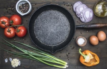 concept of cooking scrambled eggs, tomatoes, bell peppers, red onions, butter, eggs, green onions, garlic, lined around a vintage frying pan, on a wooden rustic background, space for textの写真素材
