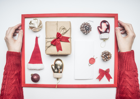 girl in red sweater hugs frame, Christmas or New Year composition, Santa Claus hat, lollipops, gift in box with bow, red wrapping paper, lined on white background, top view, flat layの写真素材
