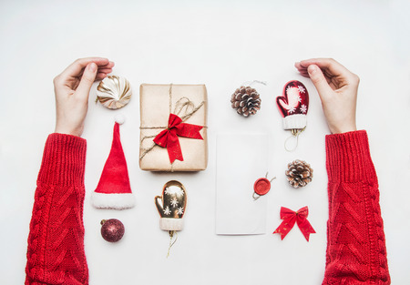 girl in red sweater hugs, Christmas or New Year's composition, Santa Claus hat, lollipops, gift in box with bow, red packing paper, lined on white background, top view, flat layの写真素材
