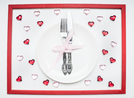 composition for Valentine's day knife and fork tied with ribbon on a plate with decorative hearts frameの写真素材