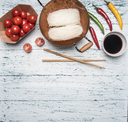 concept preparation of Funchoza with hot pepper, tomatoes and soy sauce, on a light rustic wooden background, space for textの写真素材