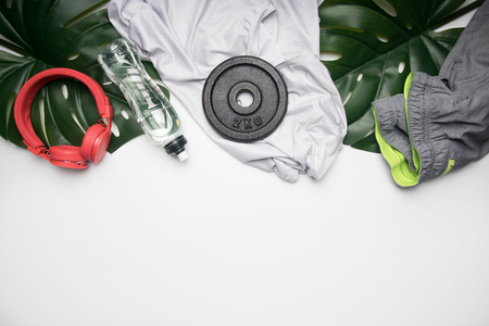 concept of sports lifestyle, sportswear and accessories lined up on a white background, with a bottle of water and tropical leaves, space for textの写真素材