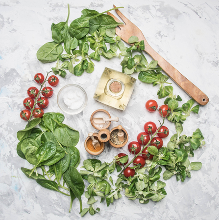 Concept of cooking vegetarian food, cherry tomatoes, various salad varieties, spinach seasonings, spices, olive oil, salad fork, space for textの写真素材