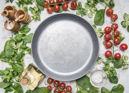 Concept of cooking vegetarian food, cherry tomatoes, various salad varieties, seasonings, spices, olive oil, lined around a vintage frying pan place for textの写真素材