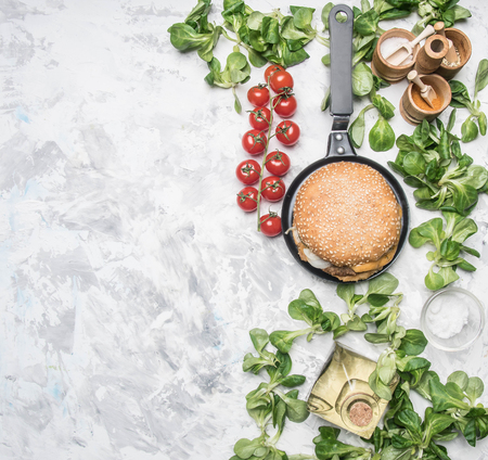 cooking a homemade burger with chicken cutlet, and a side dish of salad with cherry tomatoes, seasonings and oil, on a white rustic vintage background place for textの写真素材