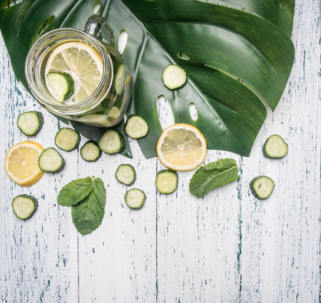 cooking healthy lemonade with cucumber, lemon and mint on a white rustic wooden background, with a tropical leaf, top viewの写真素材