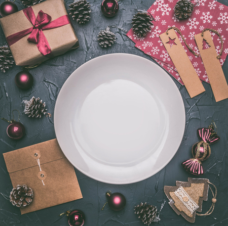 Christmas concept, postcard, gift box, Christmas toys and cones, on a grey background, lined around a white plateの写真素材