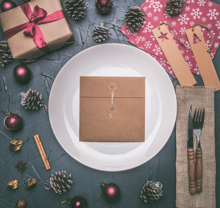 Christmas concept, postcard, gift box, Christmas toys and cones, on a grey background, lined around a white plateの写真素材