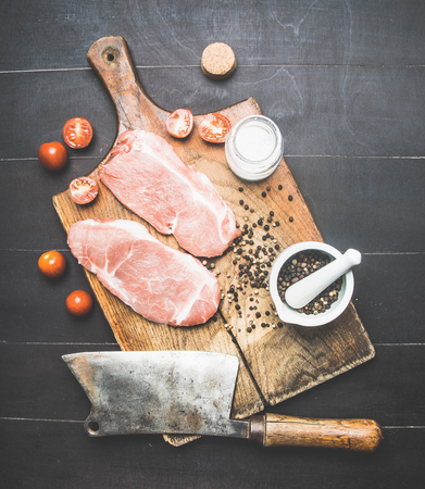 two delicious raw pork steaks on a vintage cutting board with meat cleaver, spices and tomatoes, top viewの写真素材