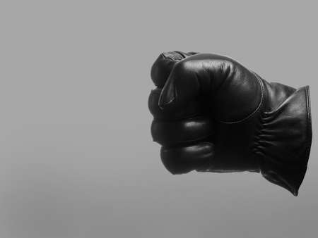 black leather glove shows clenched fist left gesture. isolated neutral background. copy space