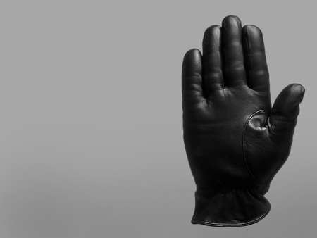 black leather glove shows open palm up to yourself gesture. isolated neutral background. copy space