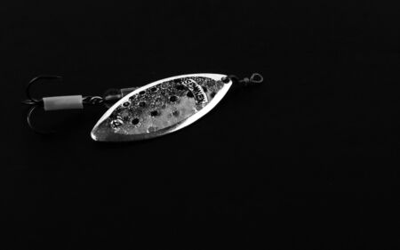 An exhibition of pirated copies of fishing metal spoon baits. Bait for fishing in the shape of a spoon with a hook on a black background.の写真素材