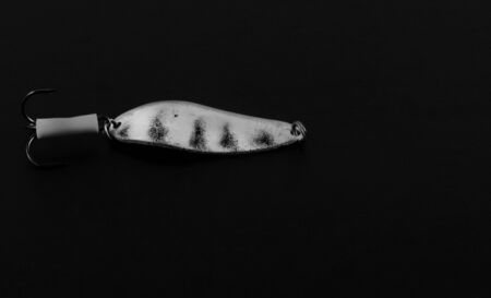 An exhibition of pirated copies of fishing metal spoon baits. Bait for fishing in the shape of a spoon with a hook on a black background.の写真素材