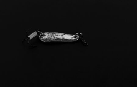 An exhibition of pirated copies of fishing metal spoon baits. Bait for fishing in the shape of a spoon with a hook on a black background.の写真素材