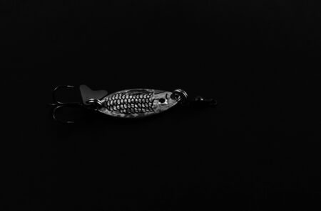 An exhibition of pirated copies of fishing metal spoon baits. Bait for fishing in the shape of a spoon with a hook on a black background.の写真素材