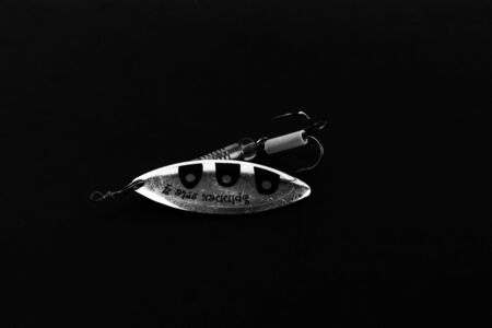 An exhibition of pirated copies of fishing metal spoon baits. Bait for fishing in the shape of a spoon with a hook on a black background.の写真素材