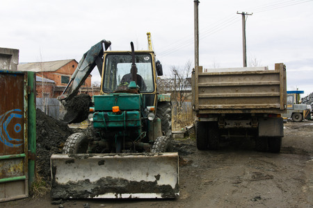 An old Soviet tractor digs and loads waste stone processing near the shop